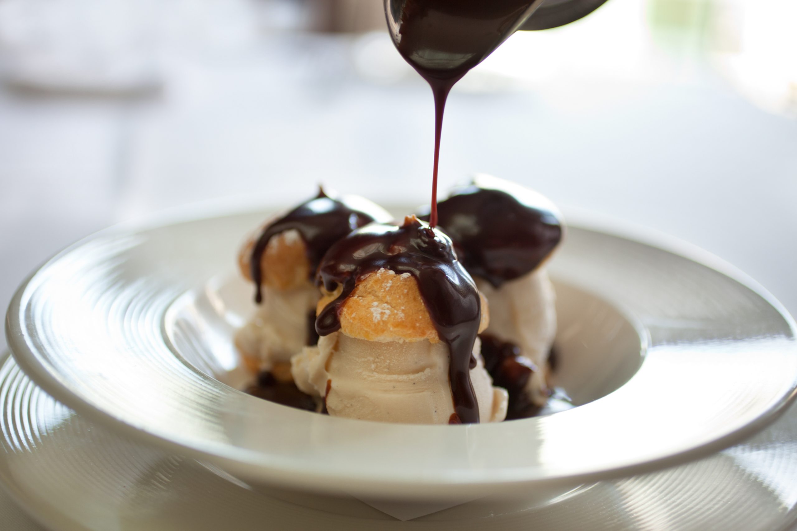 profiteroles filled with ice cream being drizzled with chocolate sauce