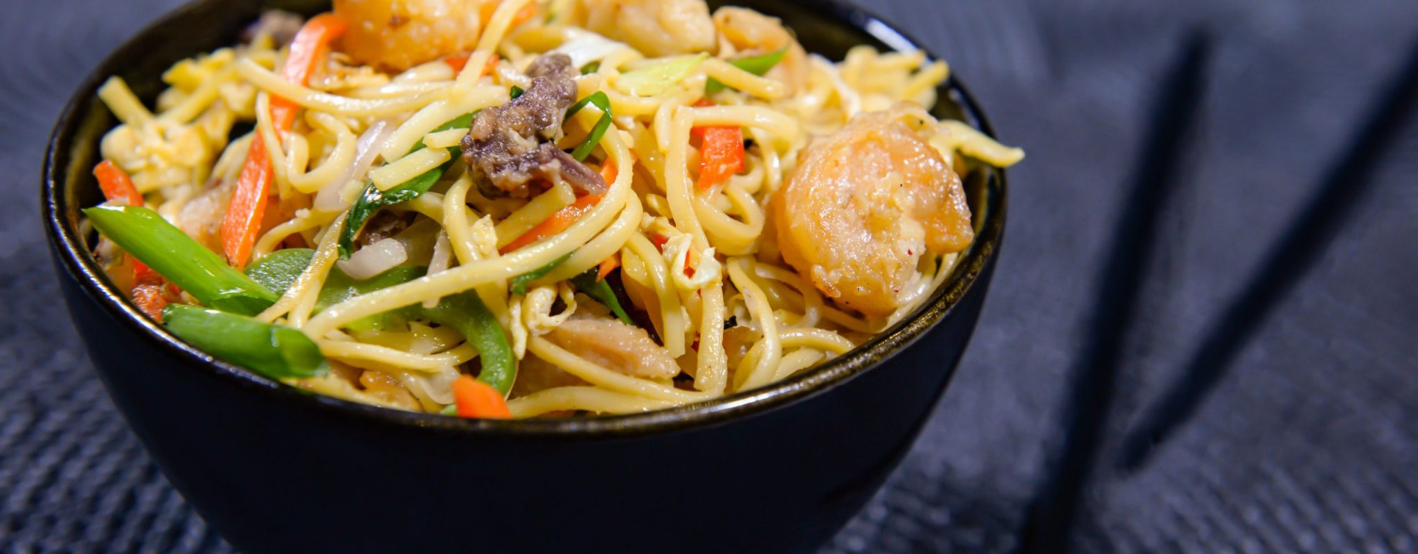 mixed fried noodles with with chicken, carrot, spring onion, bell pepper, egg and chopsticks served in bowl side view of chinese food