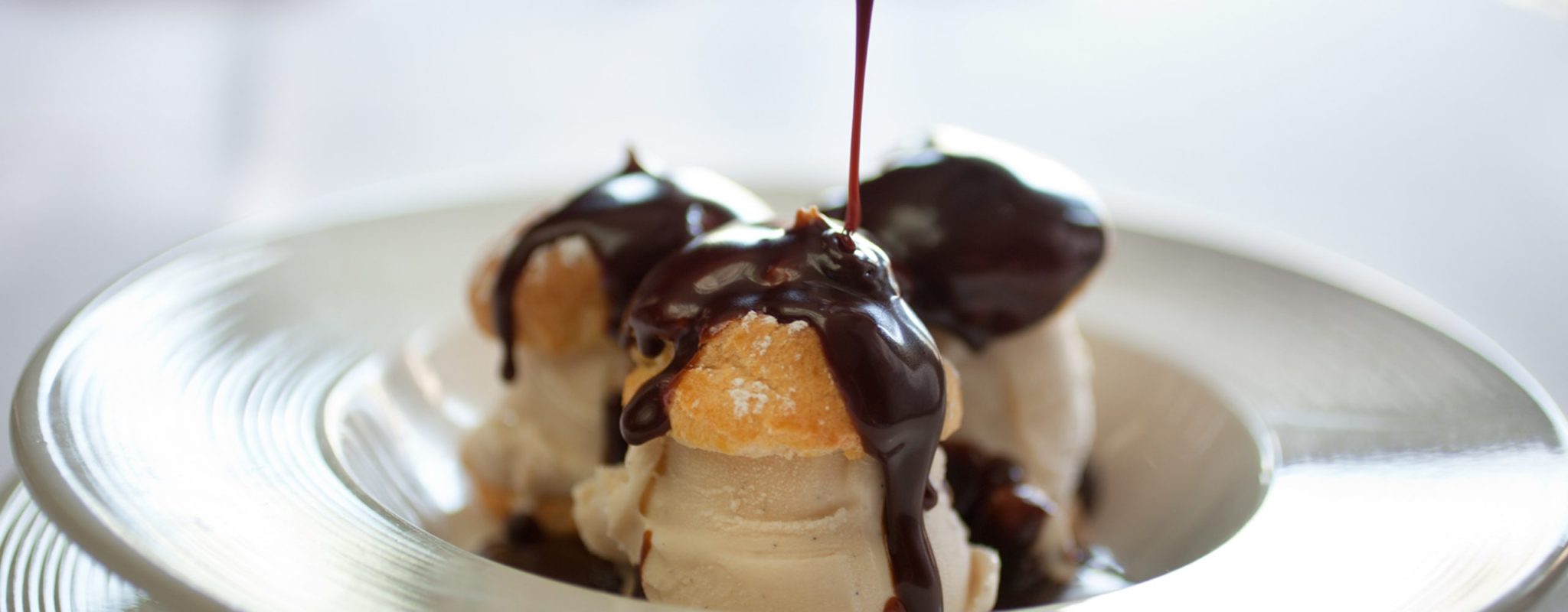 profiteroles filled with ice cream being drizzled with chocolate sauce